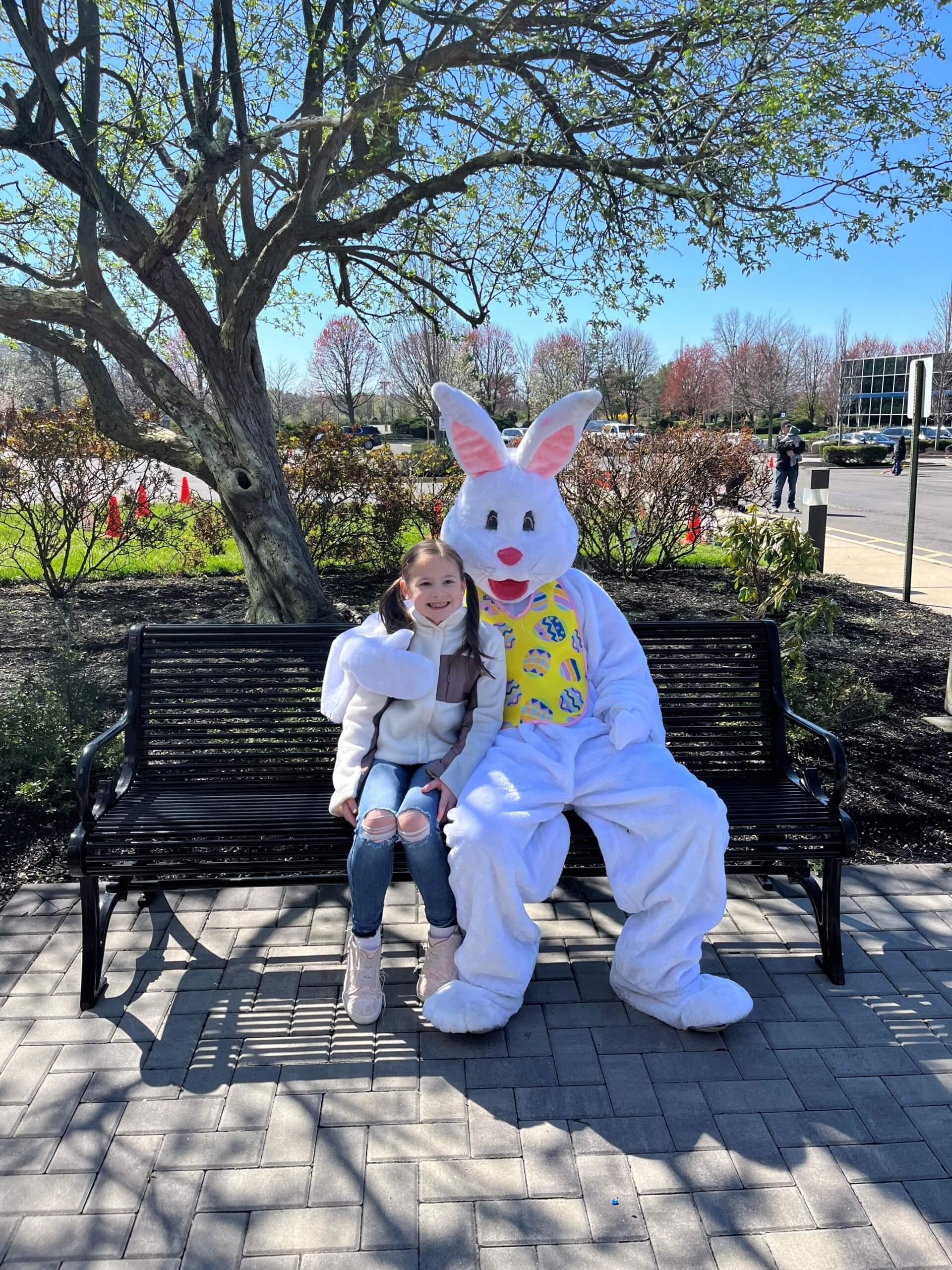 Little girl sitting on bench next to person with full easter bunny suit