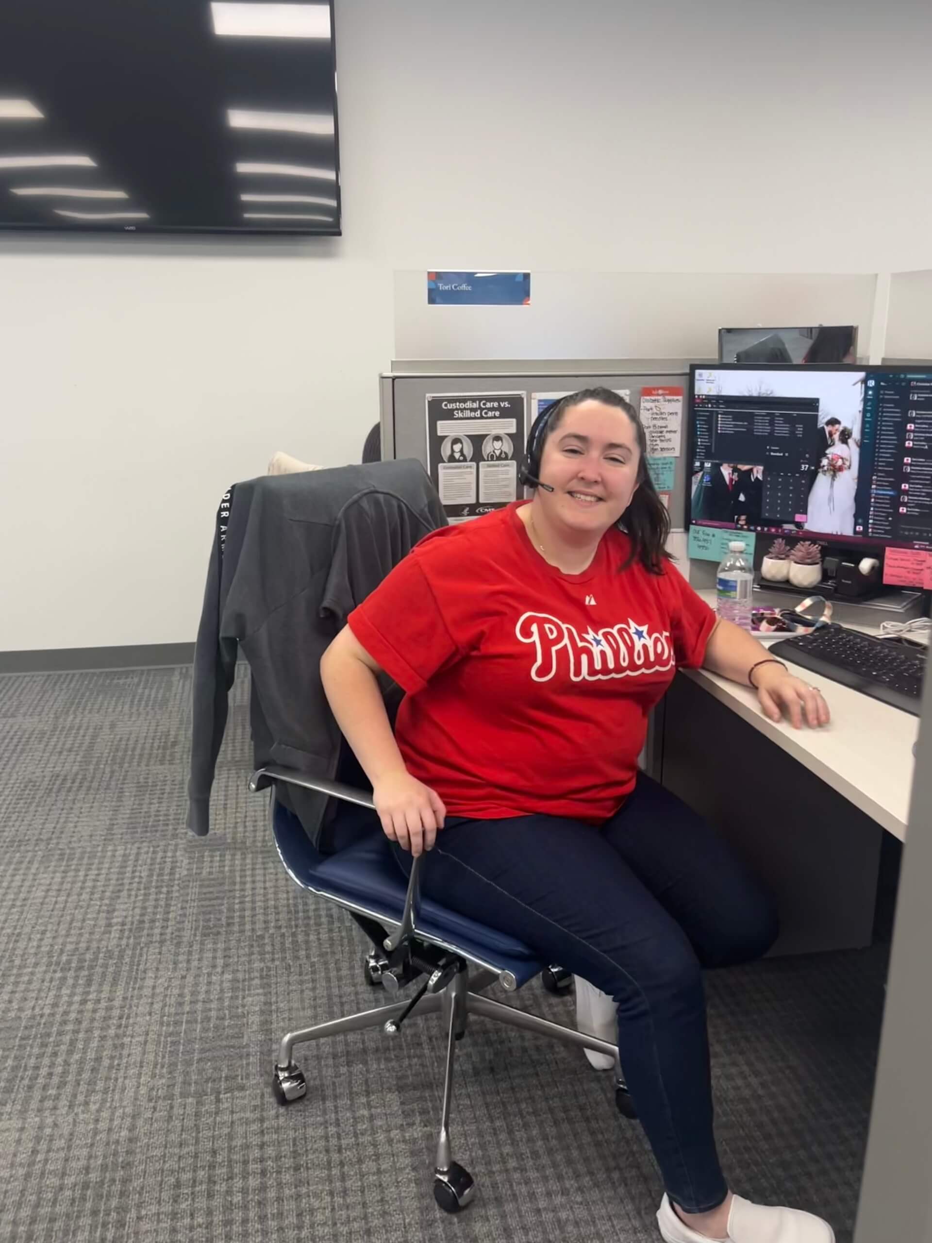 Tori Coffee in Phillies t-shirt, smiling at office desk