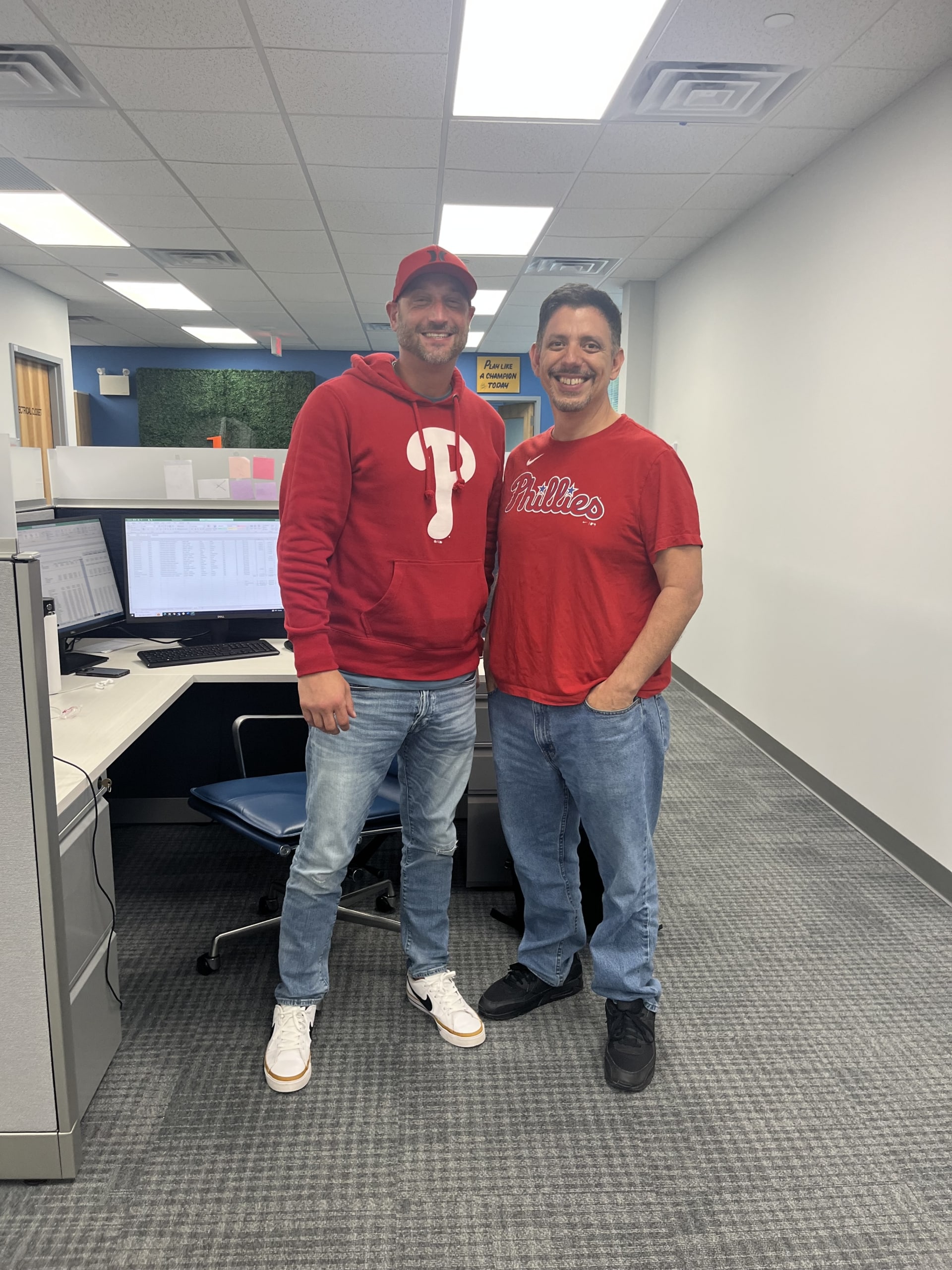 Two employees wearing Phillies merch and standing side-by-side in office