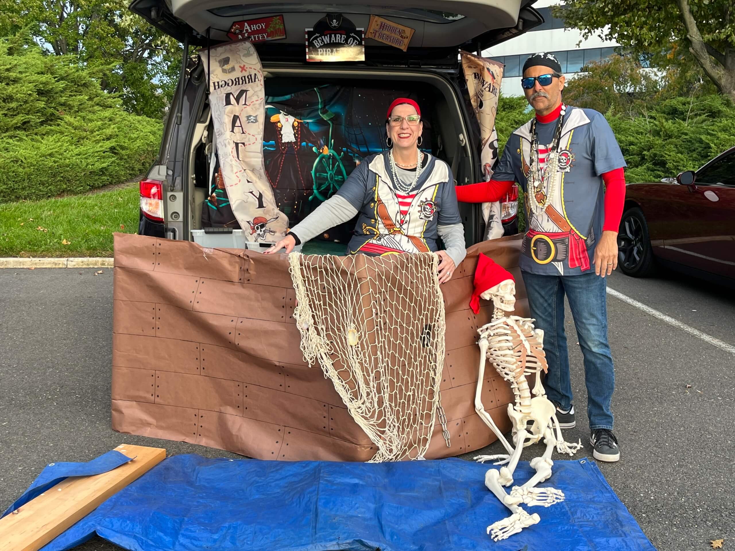 Couple dressed as pirates posing in front of their decorated car trunk