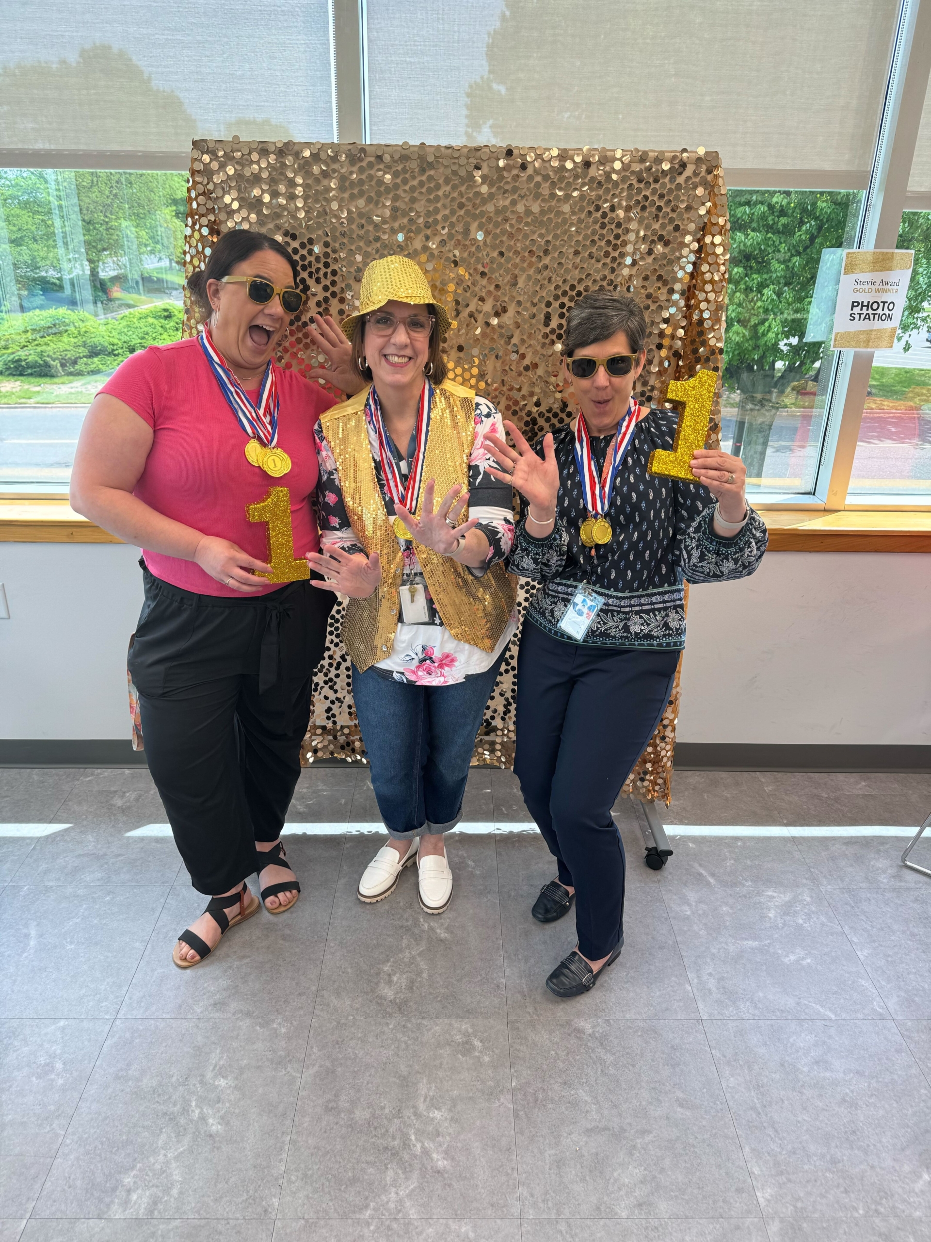 Group of ladies at an event in front of a gold wall holding golden number ones