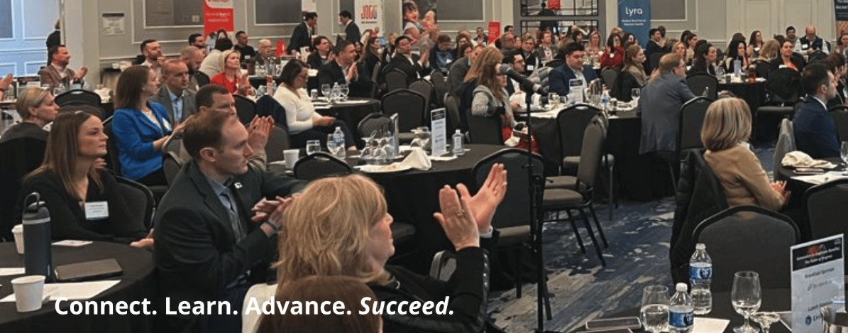 large group of people sitting at tables clapping at a conference
