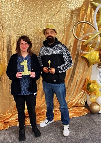 Two people posing at a event in front of a gold wall